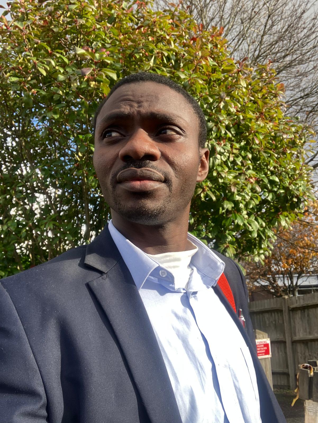 Pastor Samuel Yakubu in a suit beside a tree